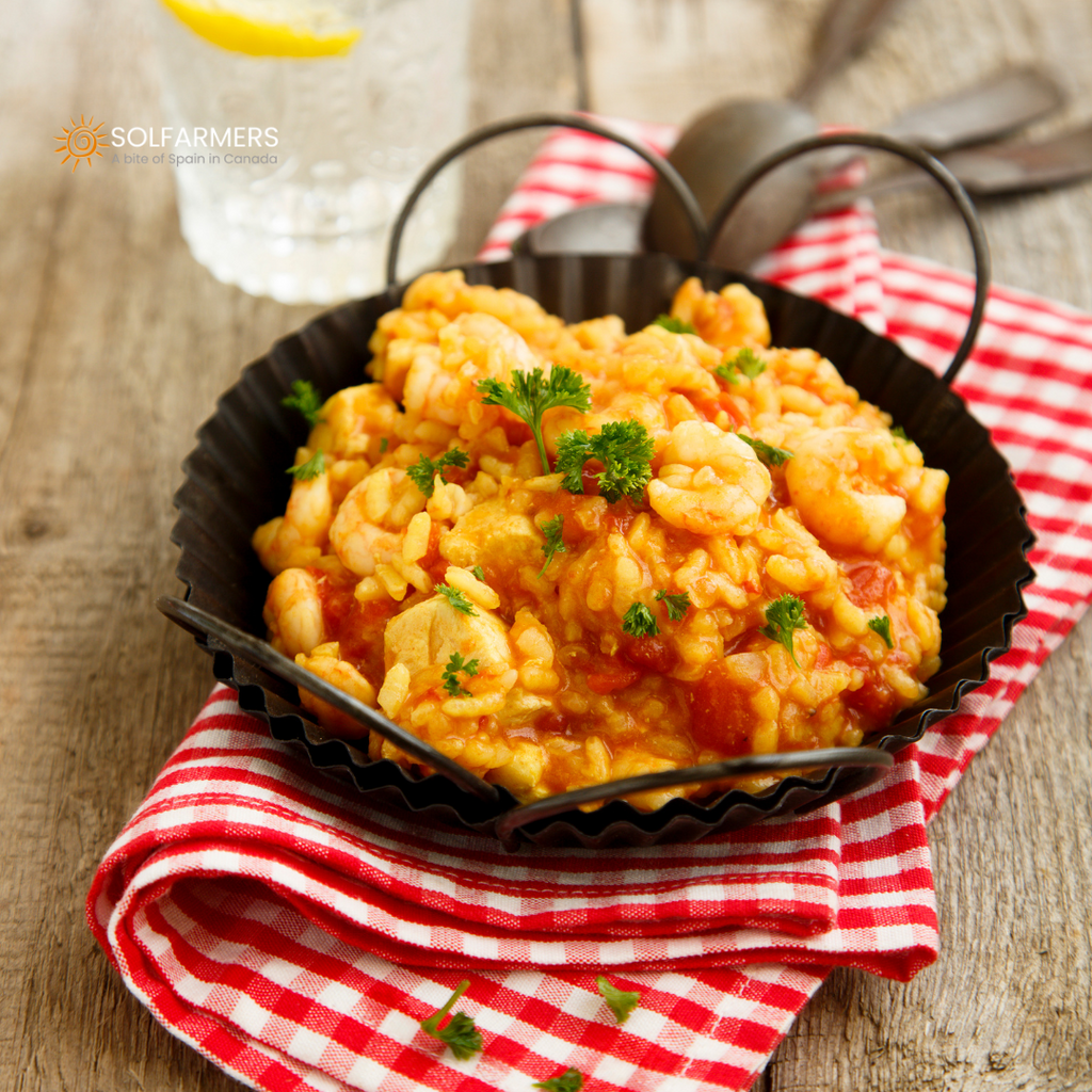 Paella with rice, broth and calamari: golden, loose rice cooked with tender calamari, all in a large paella pan with a clear broth visible and garnished with a few sprigs of parsley.