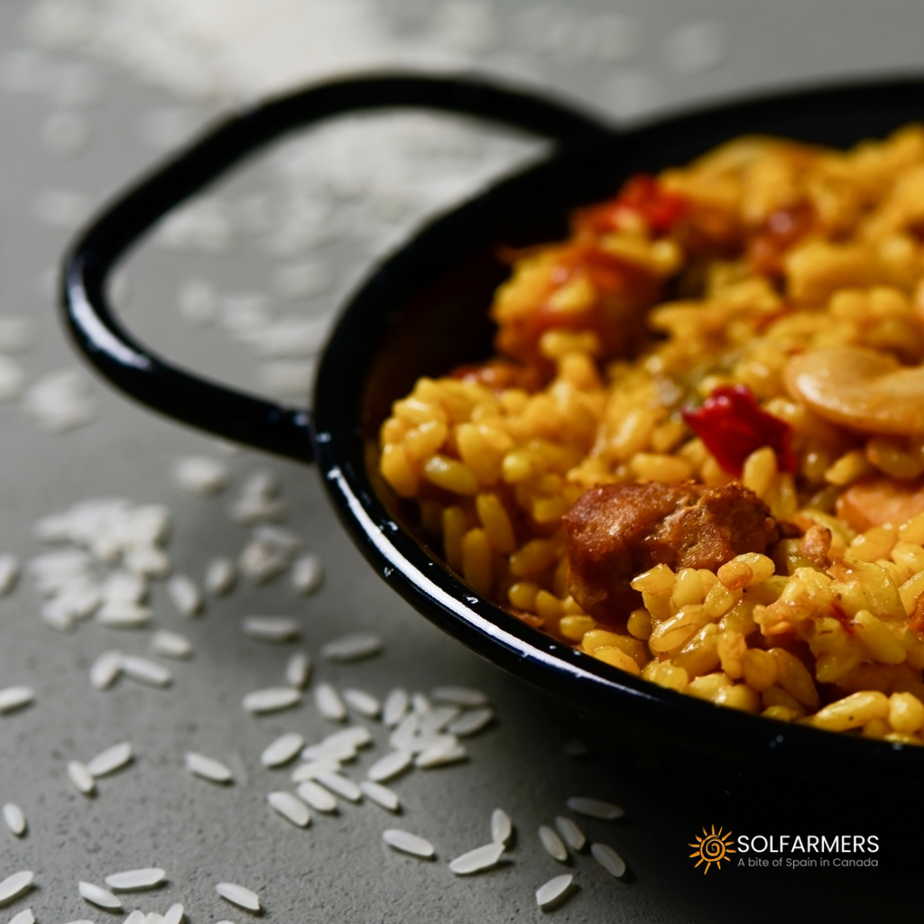 Paella de carne: colorful mixture of yellow rice with pieces of chicken, pork and chorizo sausage, accompanied by red peppers, peas and tomatoes, all cooked in a large paella pan and garnished with lemon slices and fresh parsley.