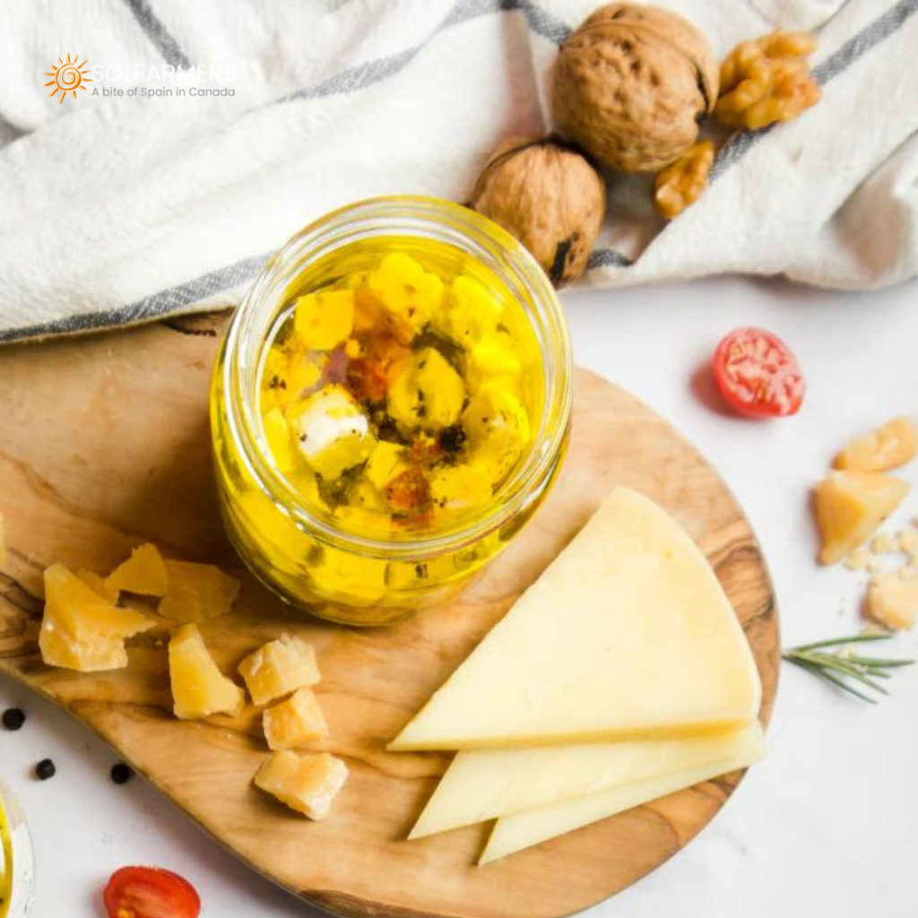 Oil-cured cheese presented in a small glass jar, with pieces of cheese firmly submerged in oil flavored with herbs and spices. The cheese shows a firm texture and golden color, while the oil reflects the infused flavors.