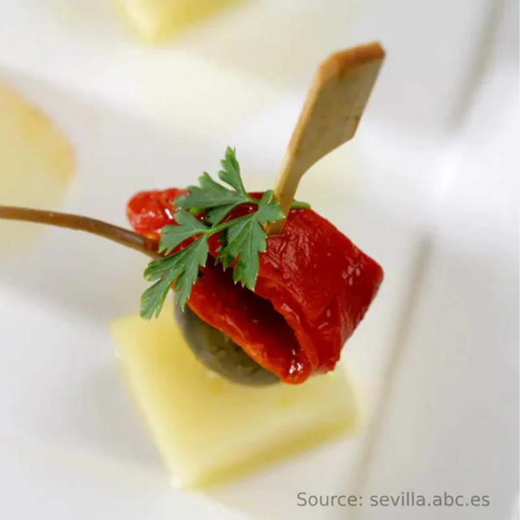 Skewers of Iberian cheese, colorful bell peppers, and capers served on a plate. The image shows cubes of Iberian cheese, red and green bell pepper chunks, and capers arranged on wooden skewers, garnished with fresh herbs and a light dressing.