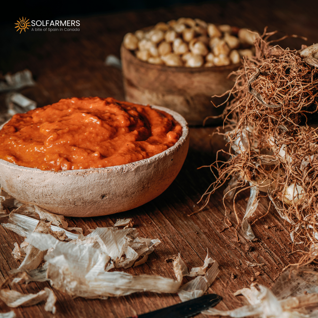 Bowl with romesco sauce: thick, red sauce, made from tomatoes, red peppers and almonds, served in a white bowl with a spoon on the side."